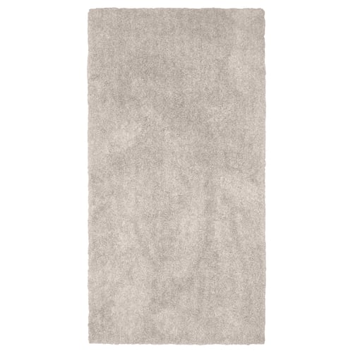 A rectangular, beige LINDKNUD rug. Made from recycled polyester, it has a soft, plush surface ideal for bedrooms.