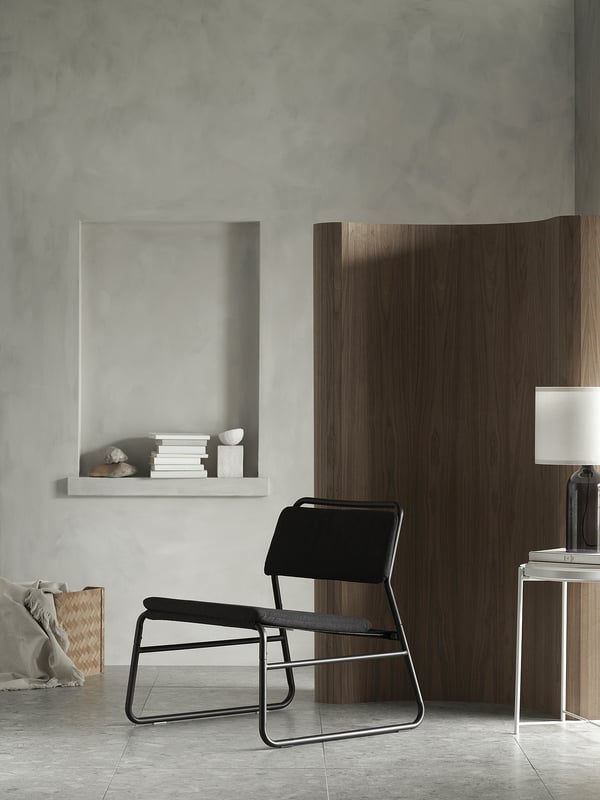 Modern minimalist room featuring LINNEBÄCK black easy chair, wooden partition, white shelf with books, and grey walls.
