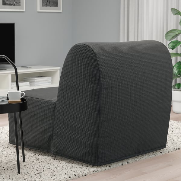Grey chair-bed on rug, black side table with coffee cup.
