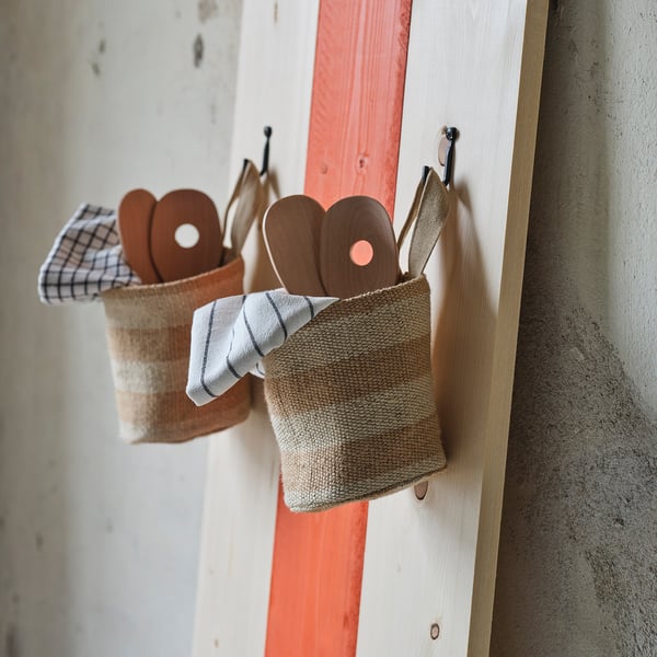 MÄVINN jute basket hangs with wooden spoons on red and white boards.