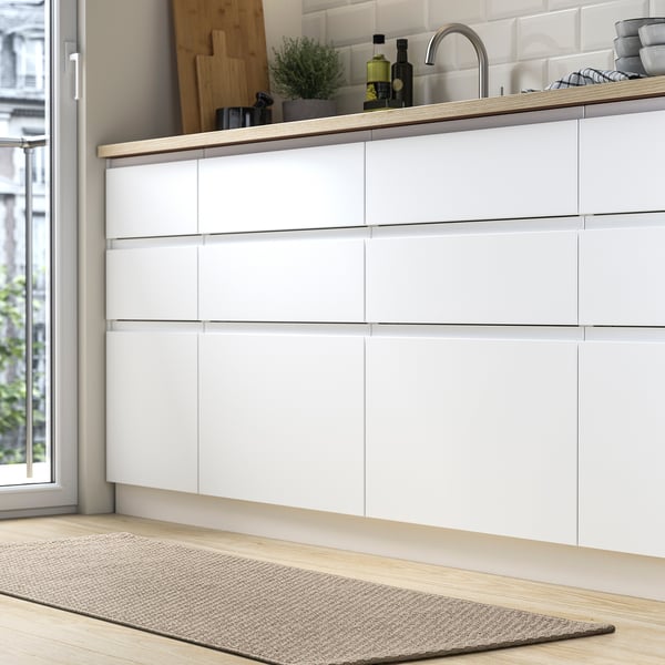 Modern kitchen with sleek white drawers, a light wood rug runner, and a window showing greenery.