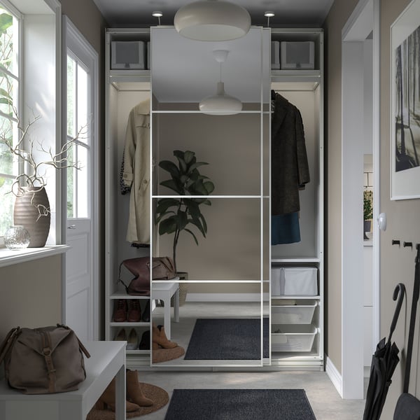Modern closet with glass doors, grey rug, hanging coats, and potted plant.