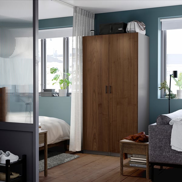 Modern bedroom: tall brown PAX wardrobe, dark wood floor, grey walls, bed, chair, and plants.