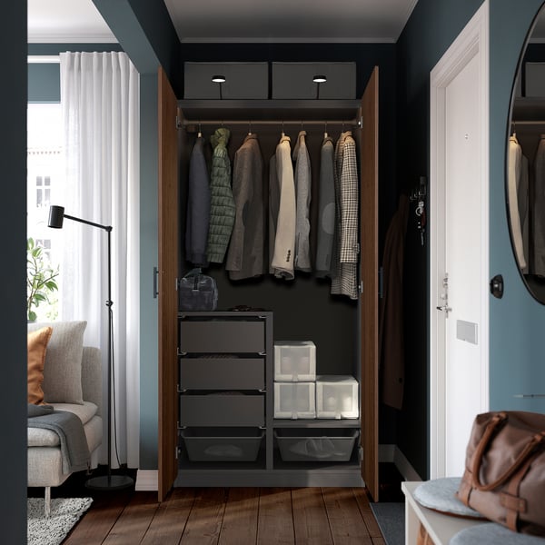 Wooden PAX closet with lights, shelves, & drawers neatly storing clothes.