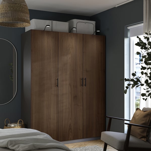 Modern bedroom with dark PAX wardrobe, large bins, circular mirror, woven pendant light, white bed, grey chair.