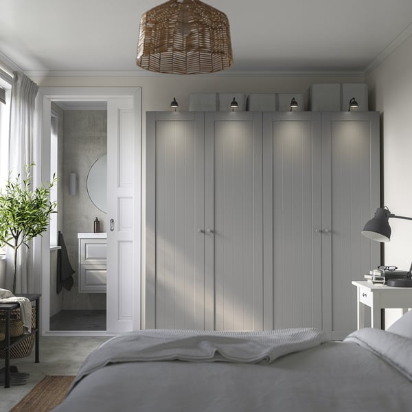 Modern bedroom with tall grey wardrobe and basketball lamp. Door to bathroom with round mirror.