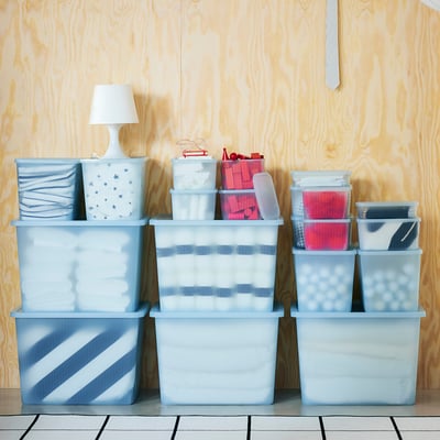 Several blue RYKTA storage boxes in varying sizes, stacked neatly. Contain small items, placed against wooden wall.