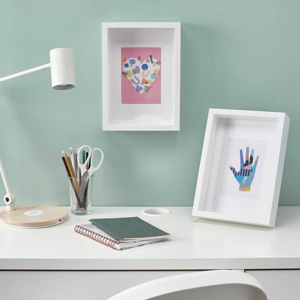 White desk, blue wall, lamp, notebooks, 2 frames
