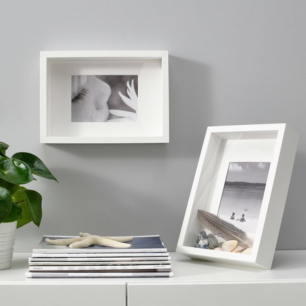 Two SANNAHED frames: one on wall, one on shelf with books, holding flower and beach photos; plant beside books.