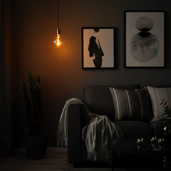 Cosy living room with SKAFTET lamp above grey sofa, abstract art, and cactus.