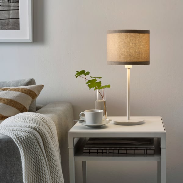 Cosy living room with SKAFTET lamp on side table, next to sofa with blanket and books.