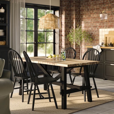 SKOGSTA black acacia wood dining set with arched chairs, woven pendant light, fruit vase, warm rug, large windows.