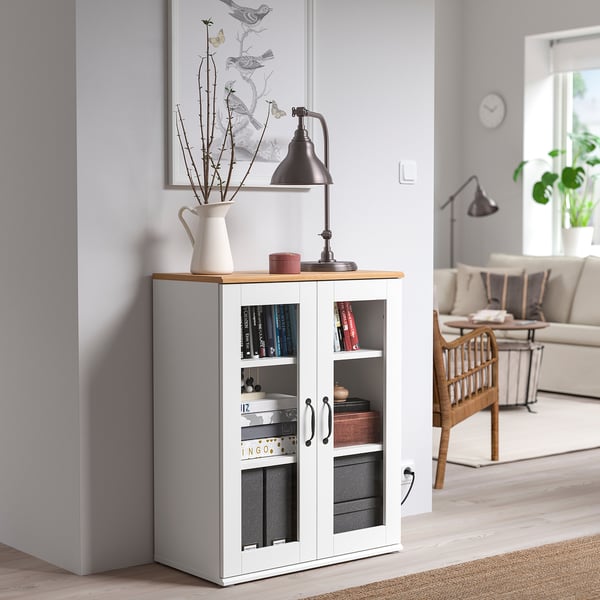 SKRUVBY glass cabinet in living room, near grey wall, holds books, lamp, and decor.