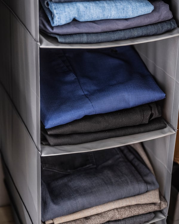 Folded clothes in SKUBB grey shelving unit, organised by colour.