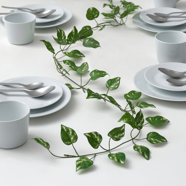 Table setting with white plates, mugs, cutlery, and artificial green plant.
