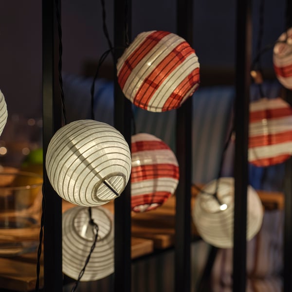 String of spherical solar lights in red, white, and translucent designs, emitting soft glow, perfect for outdoor spaces.