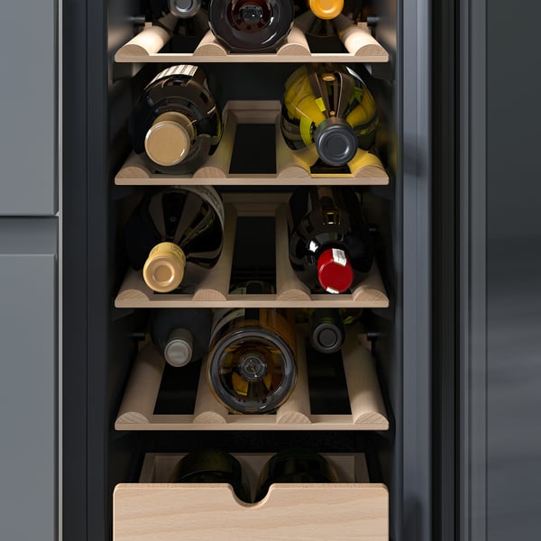 An open wine cooler with four wooden racks holding wine bottles of varying colours. Black glass door and a drawer below for additional storage.
