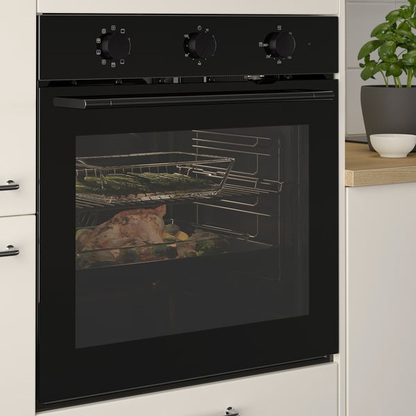 Black built-in oven with food cooking inside, featuring even heat distribution and a self-cleaning function, set in a modern kitchen.