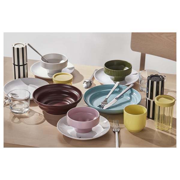 Assorted colourful ceramic bowls, cups, and modernist black and white striped spice mills displayed on a light wooden table.