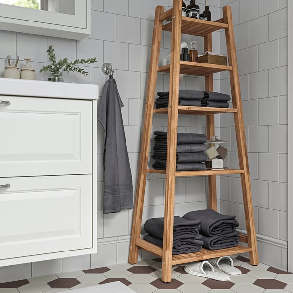 Acacia wood shelving unit in bathroom with towels and toiletries.