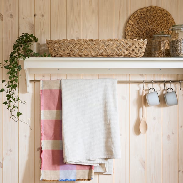Kitchen with hanging towels, mugs, spoons, and a STYLTSNÄPPA bread basket. Handwoven rattan basket sits between items.