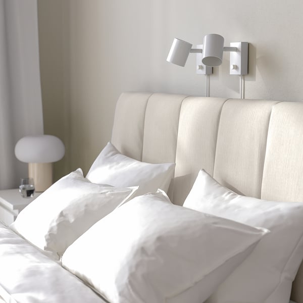 Minimalist bedroom with cream-colored bed, sleek headboard, and wall-mounted reading lamps.