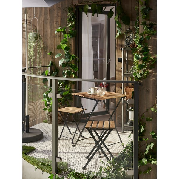 Small balcony with wooden TÄRNÖ stool & table, surrounded by greenery. The table is foldable and compact, perfect for limited spaces.