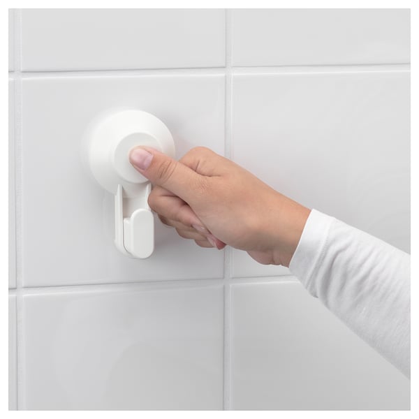 A hand pushes a white TISKEN suction hook onto a tiled wall.