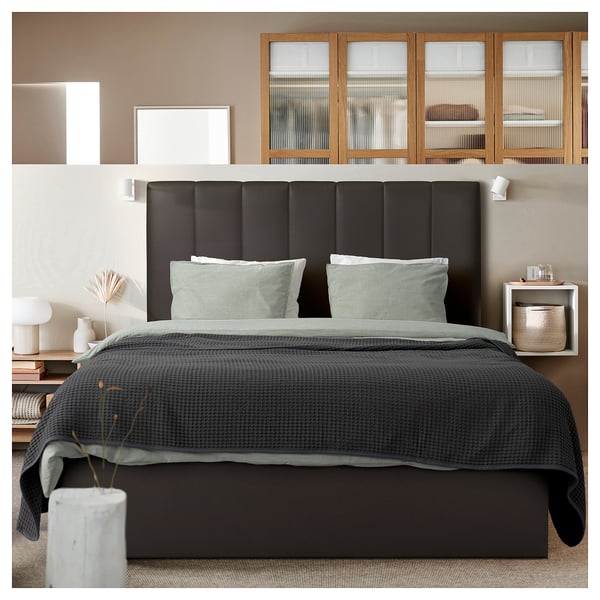 Modern bedroom with black TJÅLLE headboard, grey bedding, and wooden shelves.