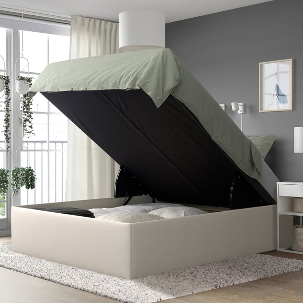Bed with TJÅLLE storage revealed by open fabric lid, showing soft-close mechanism and ample space underneath.