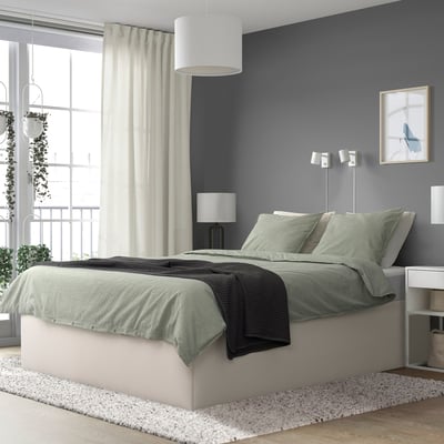 Modern bedroom with TJÅLLE bed, grey, upholstered, wide and low, beneath window, lamp, and decor.
