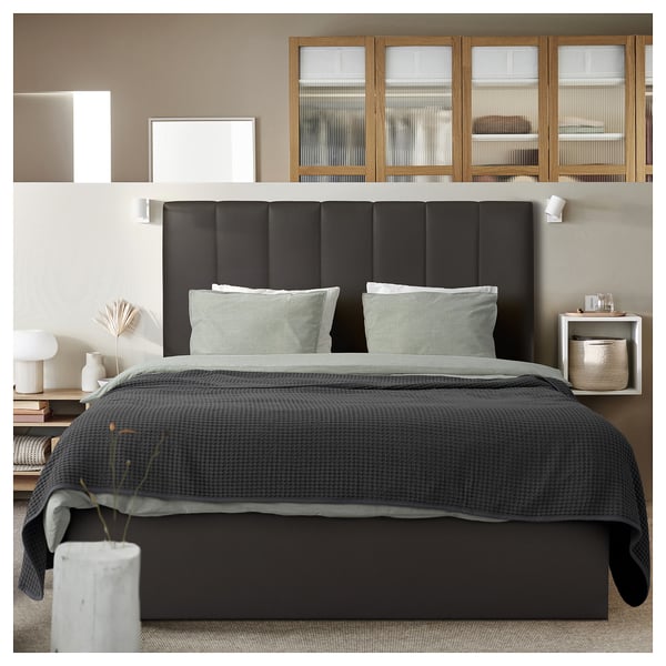 Modern bedroom with dark grey TJÅLLE bed, matching headboard, and light grey accents. Simple, stylish decor with glass cabinets and white walls.