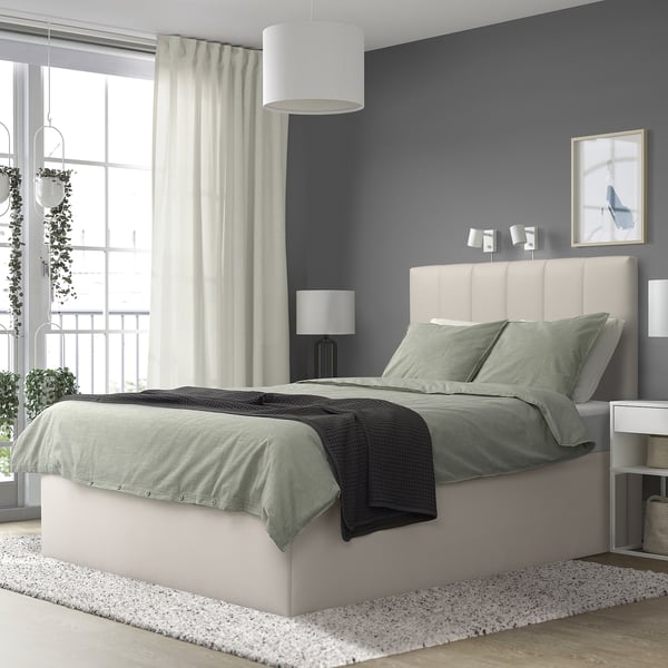 Modern bedroom with grey TJÅLLE bed, large by window, light fabric headboard, matching grey bedding. Grey walls, large curtains, hanging plants.