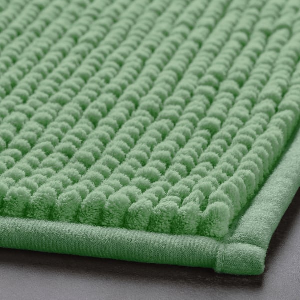 Soft green bath mat with raised dots for grip, laid on a dark surface. Feels ultra-soft and quick-drying, ensuring comfort and cleanliness.