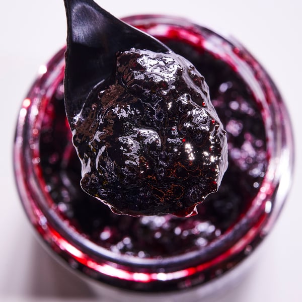 Black spoon with jam over jar.