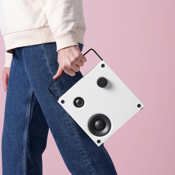 Person holding white VAPPEBY bluetooth speaker, showcasing its handle for easy portability.