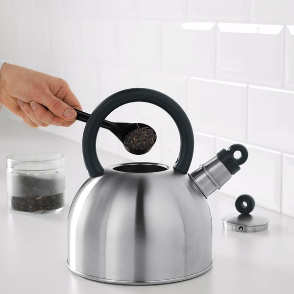 Hand pours tea leaves into whistling VATTENTÄT kettle on stove.