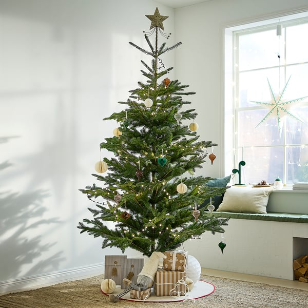 VINTERFINT christmas tree decorated with neutral ornaments and lights, near a window with gifts.