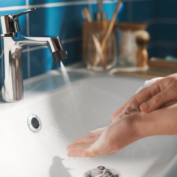Hands washing under chrome tap, blue-tiled bathroom, modern design.