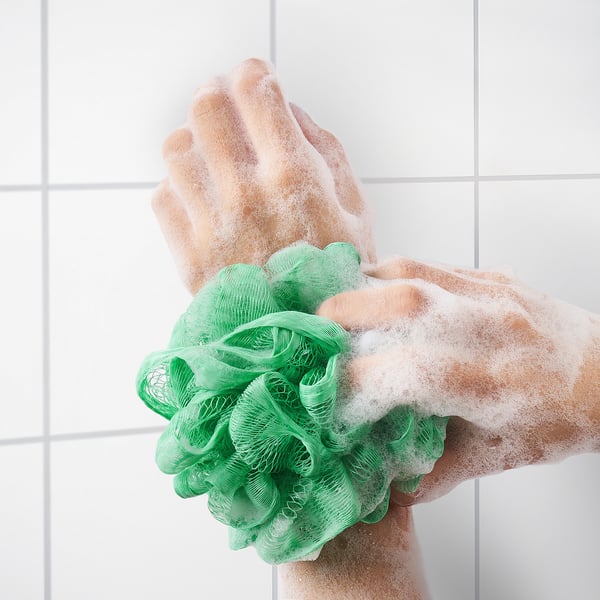 Hand using green mesh body puff with soap, exfoliating skin, creating foam.