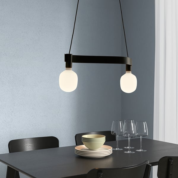 Modern dining setup with black table, chairs, ACKJA lamp, glasses, plates. Lamp is centrally placed.