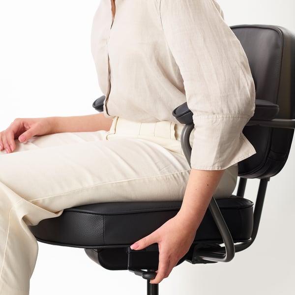 Person adjusting ergonomic office chairs armrest, showing lumbar support and leather seat.