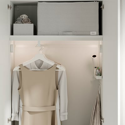 Closet with beige dress hung on rail, storage boxes, towel rolls organised in grid-patterned compartments on upper shelf.
