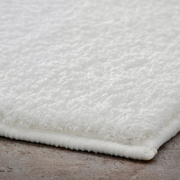 Fluffy white bath mat with dense, soft fibres, likely made of recycled materials, resting on a textured surface.