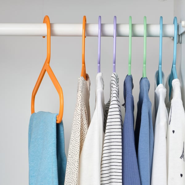 Closet with colourful hangers holding clothes; orange, purple, green, and blue hangers neatly organising garments.