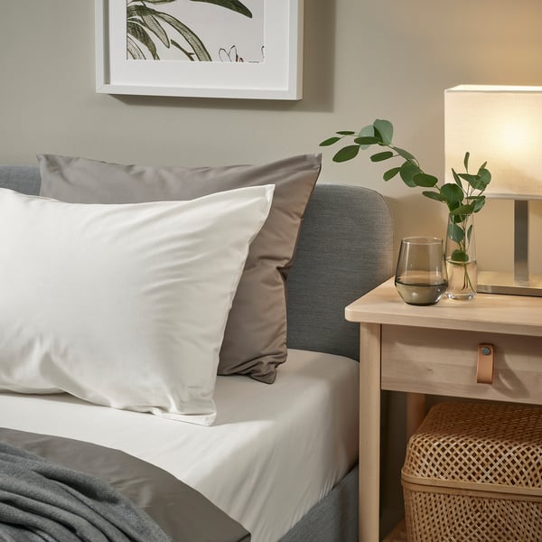 Bed with white cotton pillows, grey bedding, lamp, and plants.