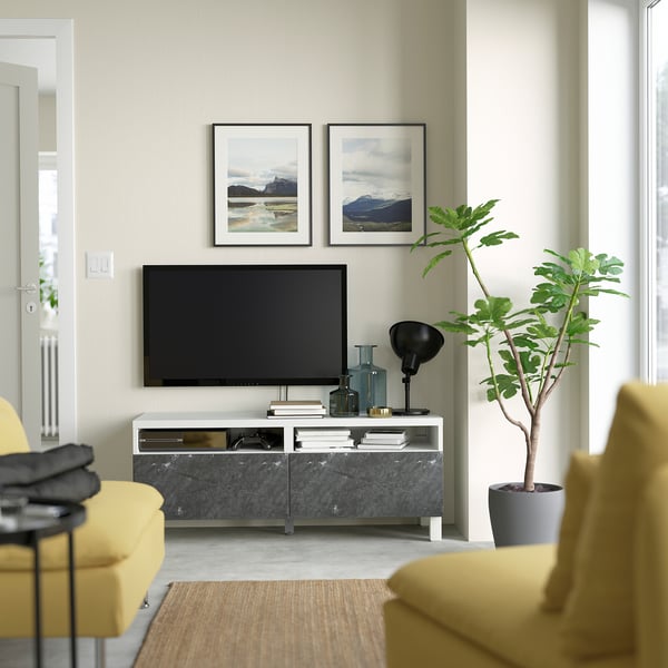 Minimalist living room with tv, mountain photos, plant, and yellow/beige chairs.