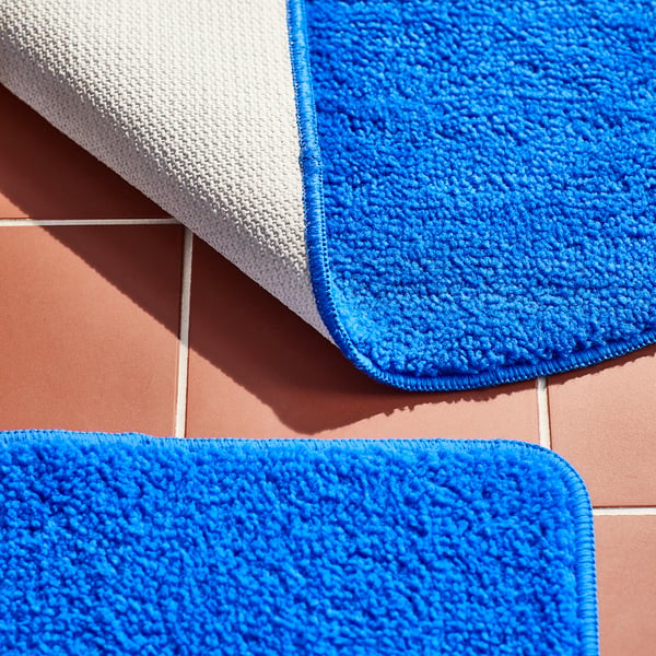 Soft, vibrant blue bathmats with textured surfaces and anti-slip backing neatly arranged on pink tiles.