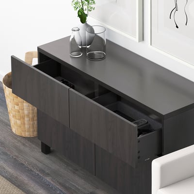 Dark wooden drawer unit with visible compartments holding remote controls and small items. Decorative vases on top.