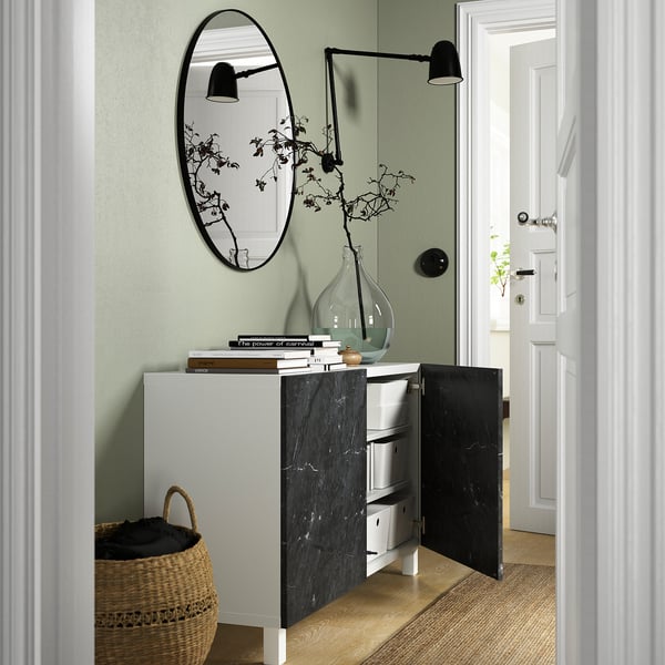 Modern room with open storage cabinet, displaying books and vase, beside a woven basket and a wall mirror.